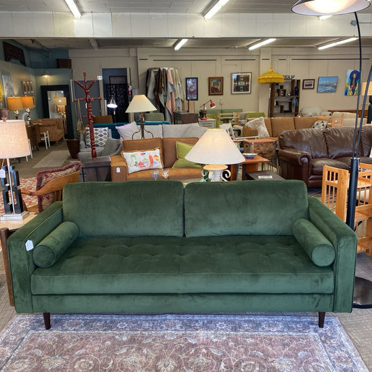Green sofa in a furniture store with various other furniture pieces in the background.