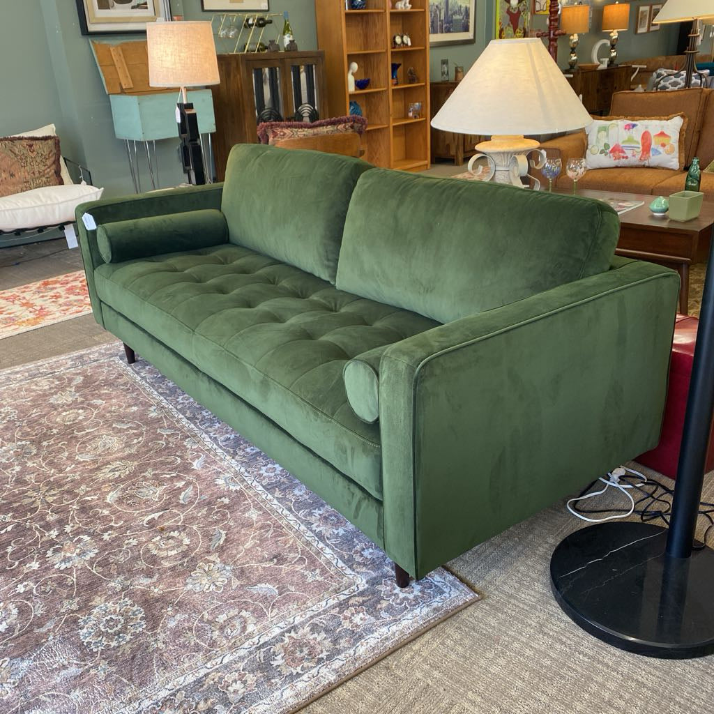 Green sofa in a living room setting with a lamp and furniture.