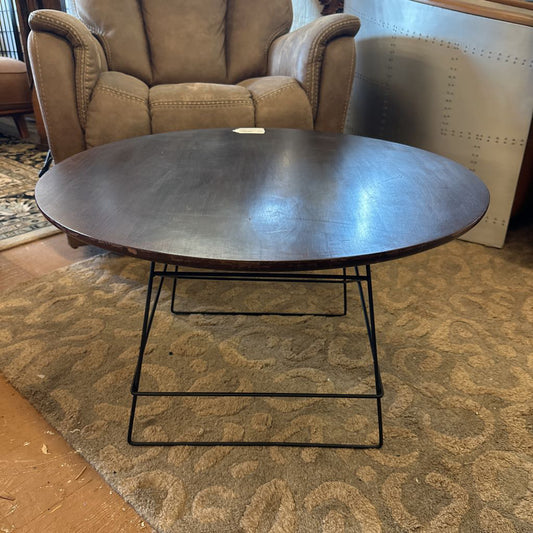 Round wooden coffee table with metal legs in a living room setting