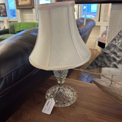 Small lamp with a beige shade and decorative base on a wooden surface.