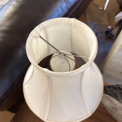 Broken lampshade with a light bulb inside on a wooden floor.