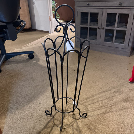 Black metal magazine rack on a carpeted floor with office furniture in the background
