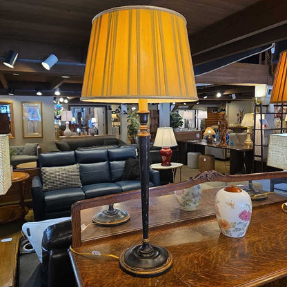 Vintage-style lamp with yellow shade on a wooden table in a store setting.