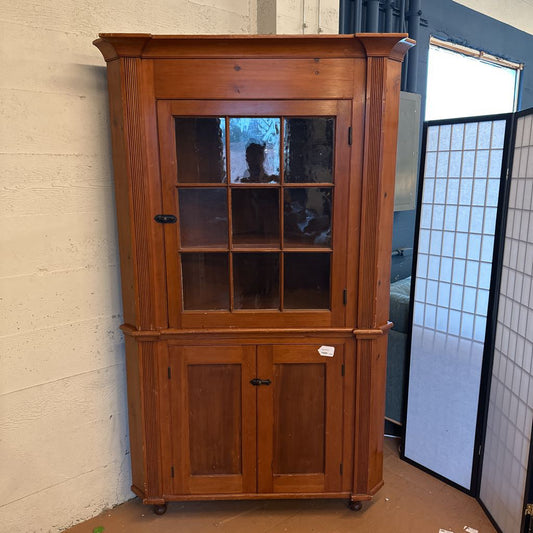 Wooden corner cabinet with glass doors and two solid doors against a neutral wall.