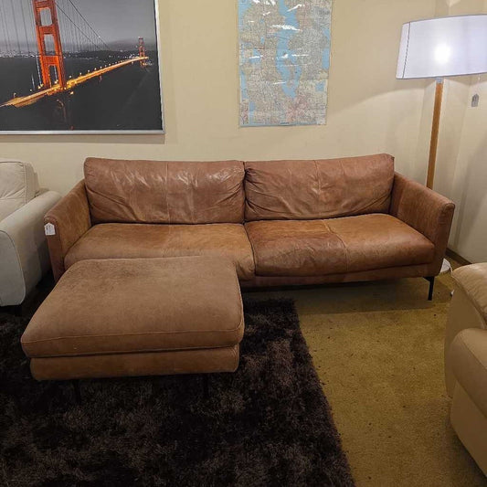 Brown leather sectional sofa in a room with a painting of the Golden Gate Bridge on the wall.