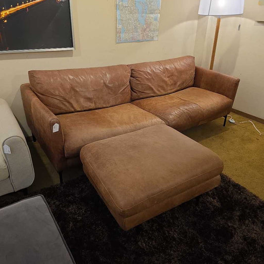 Brown leather sectional sofa with ottoman on a dark rug in a room.
