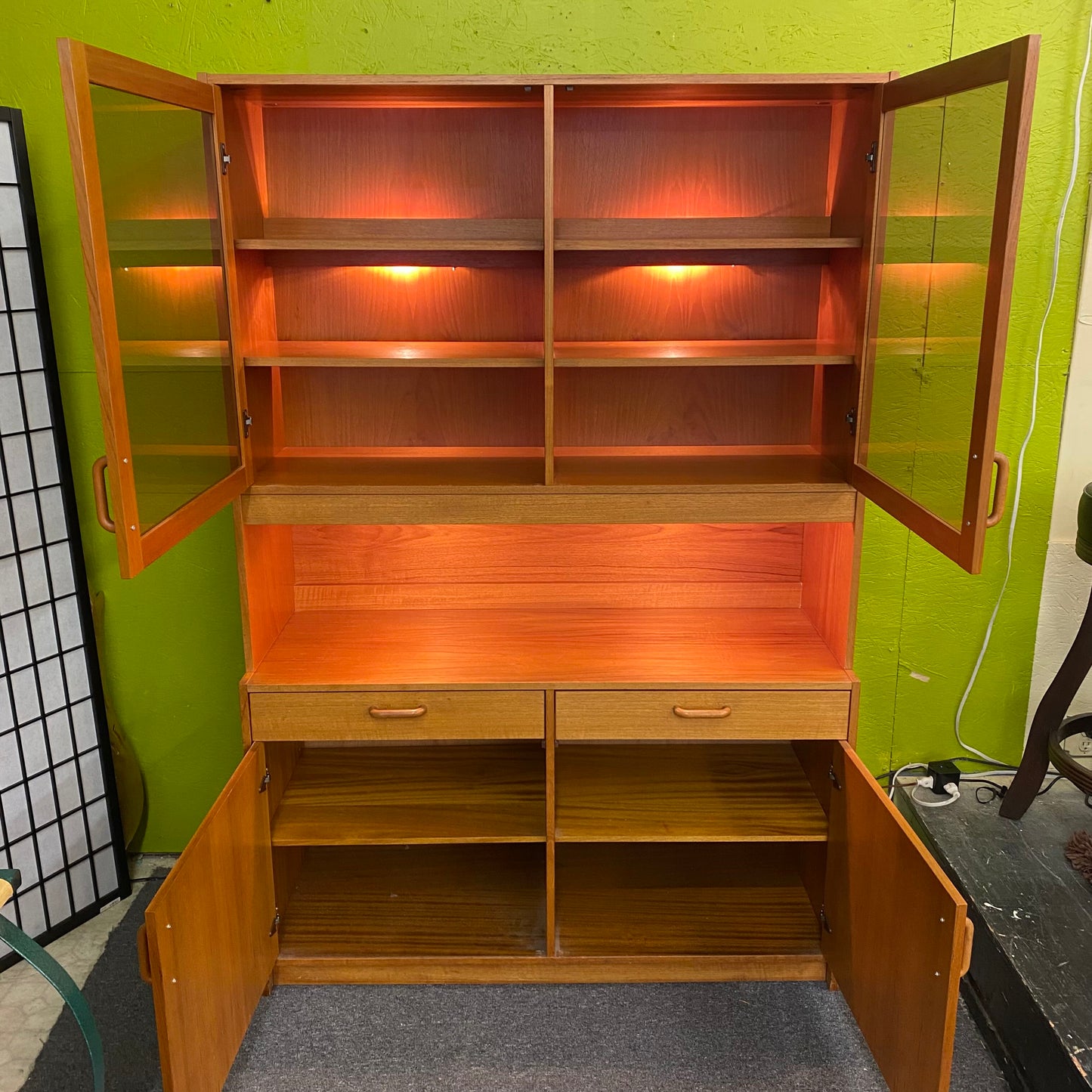 Wooden cabinet with open doors against a green wall.