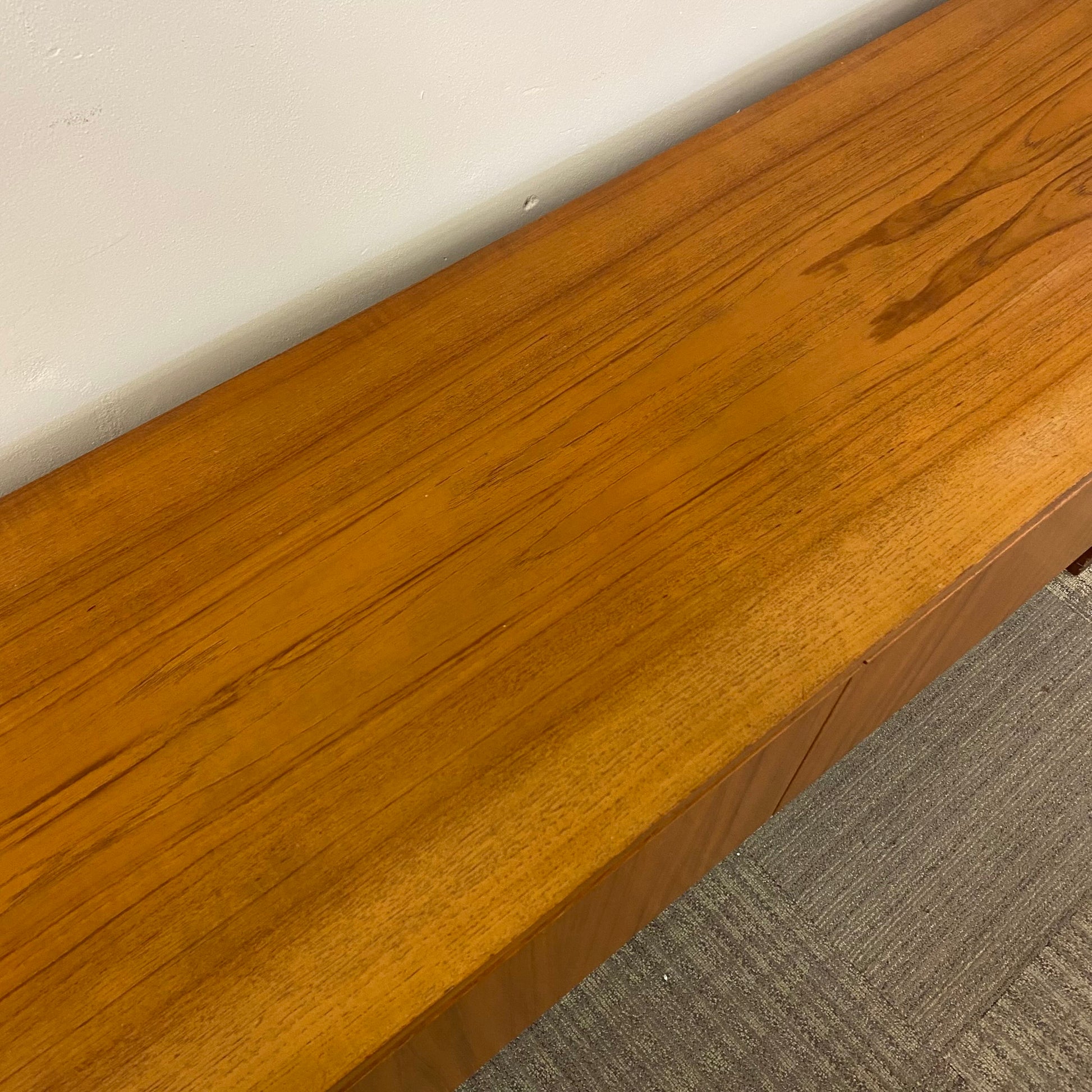 Close-up of a wooden desk edge with a white surface and gray carpet in the background