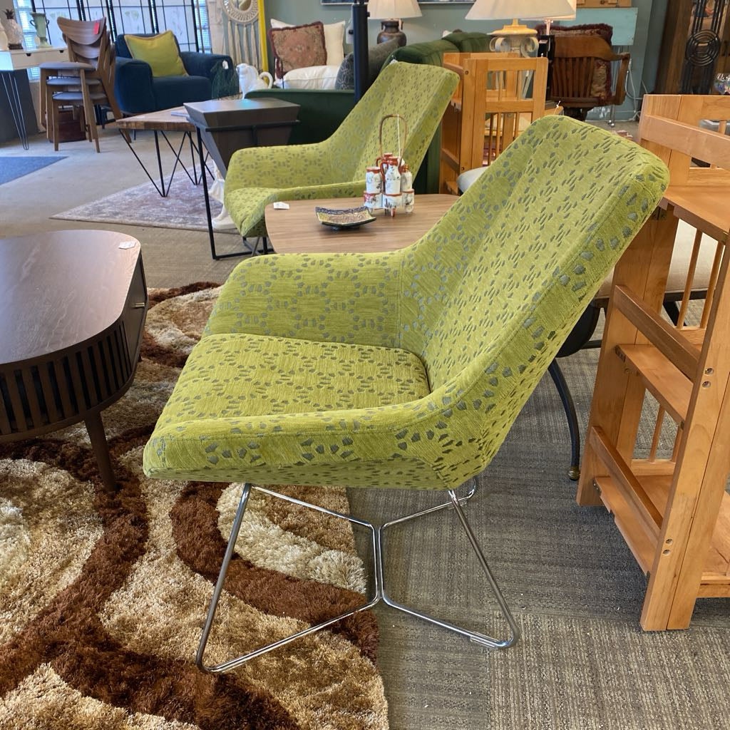 Green patterned chair in a furniture store with various chairs and tables in the background.