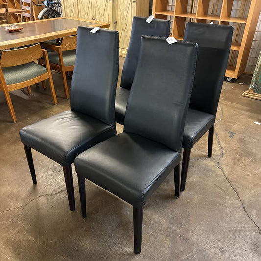 Four black chairs with tags on a concrete floor in a store setting.