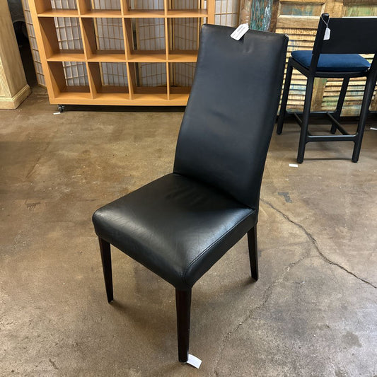 Black leather chair with a tag on a concrete floor in a storage or warehouse setting.