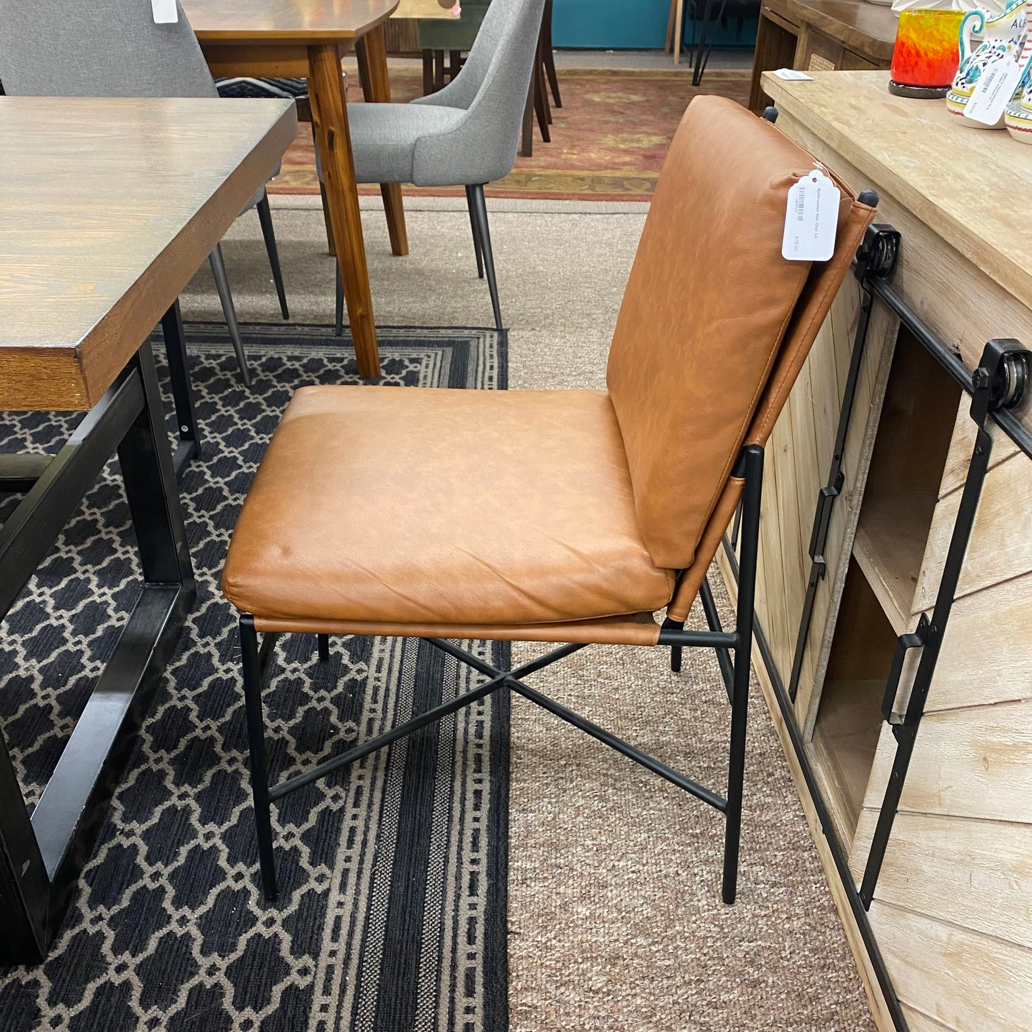 Brown leather chair with metal frame on a patterned rug in a room with tables and chairs.