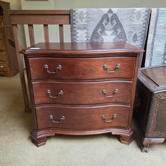 Wooden dresser with curved design and metal handles on a carpeted floor.