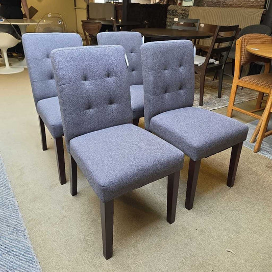 Set of gray upholstered chairs with dark wood legs in a showroom setting.