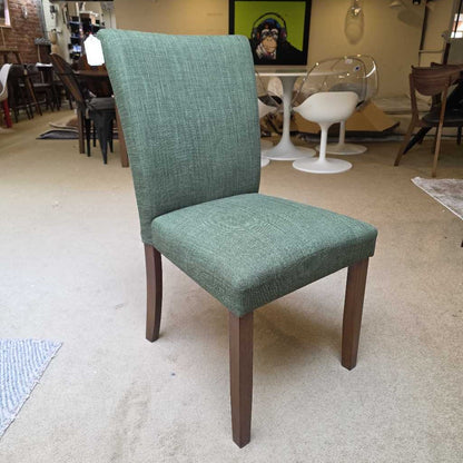 Green upholstered chair with wooden legs in a showroom setting