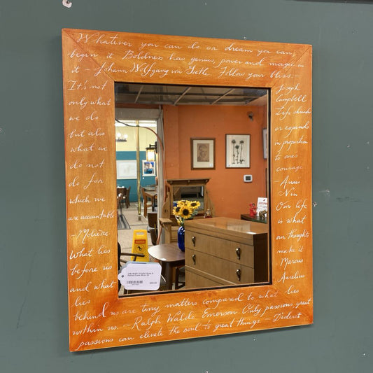 Mirror with orange frame featuring text on a gray wall