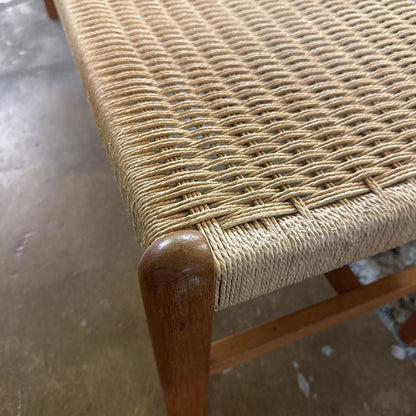 Close-up of a woven chair seat with wooden frame on a concrete floor.