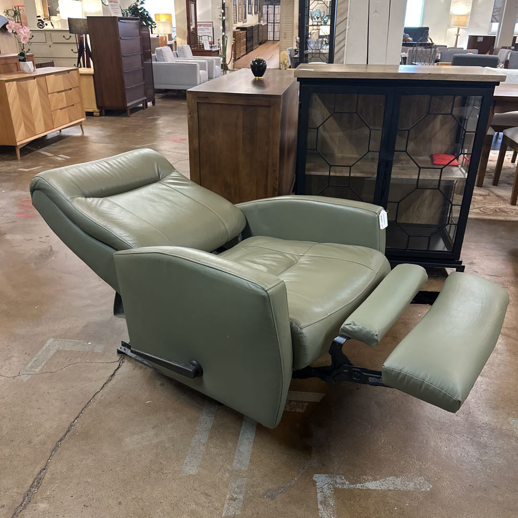 Green recliner chair in a showroom setting with furniture and decor in the background.