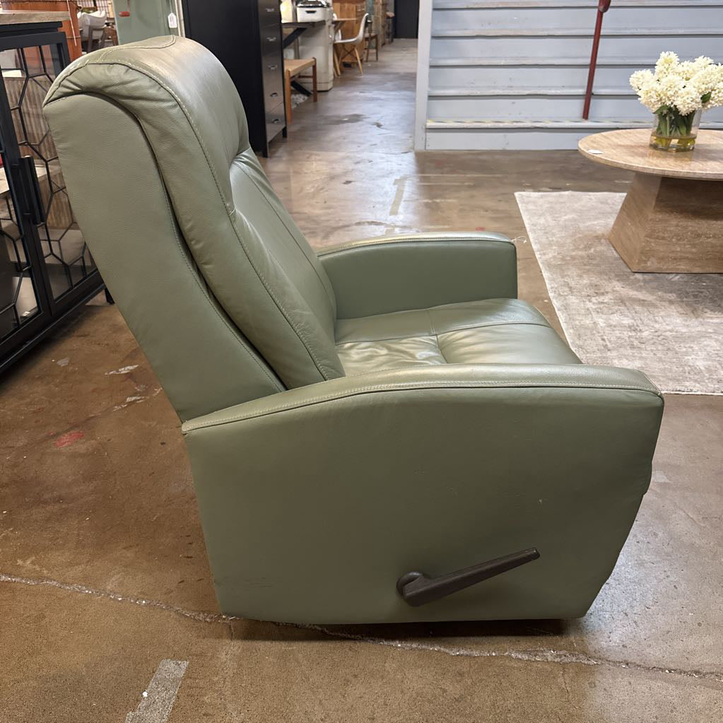Green leather recliner chair in a showroom setting with wooden flooring and tables.