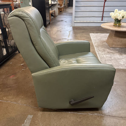 Green leather recliner chair in a showroom setting with wooden flooring and tables.