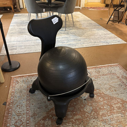 Black exercise ball chair on a patterned rug in a room with furniture.