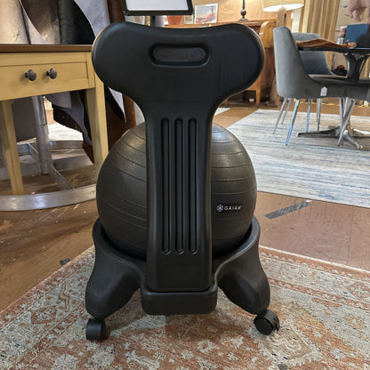 Black exercise ball chair on a patterned rug in a room with furniture.