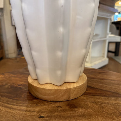 White ceramic vase on a wooden base with a blurred indoor background
