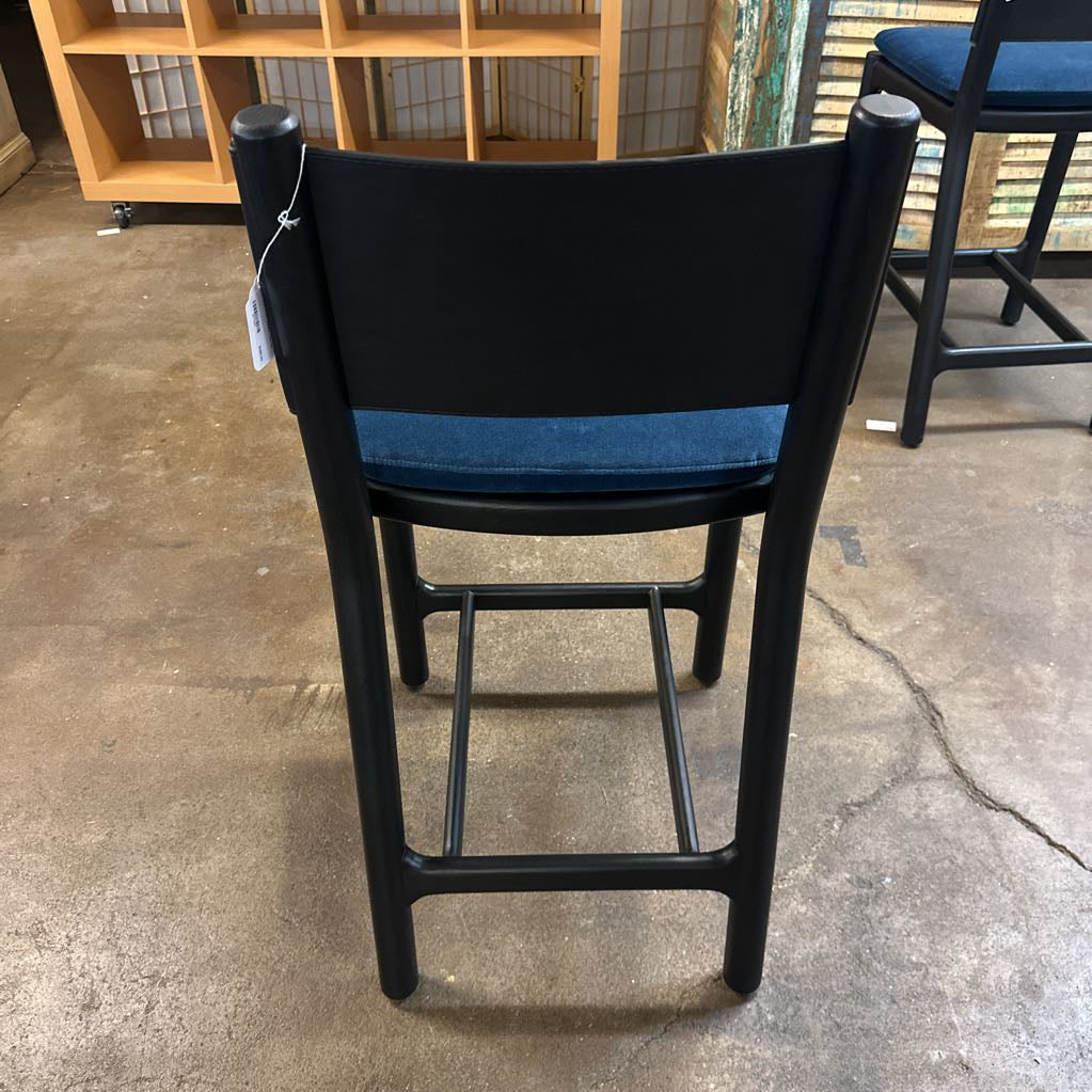 Black bar stool with blue seat on a concrete floor