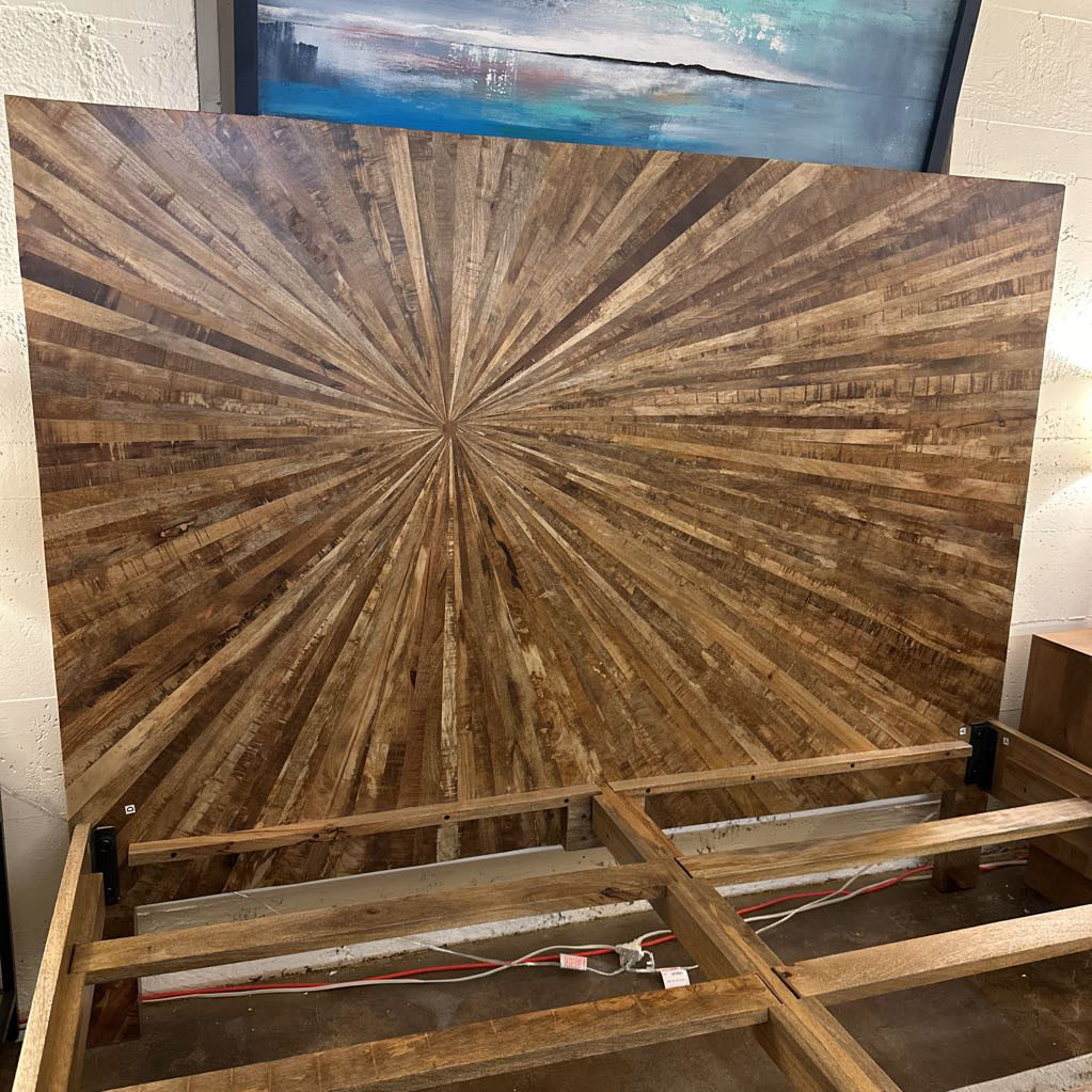 Wooden panel with starburst pattern on a stand, with a painting in the background.