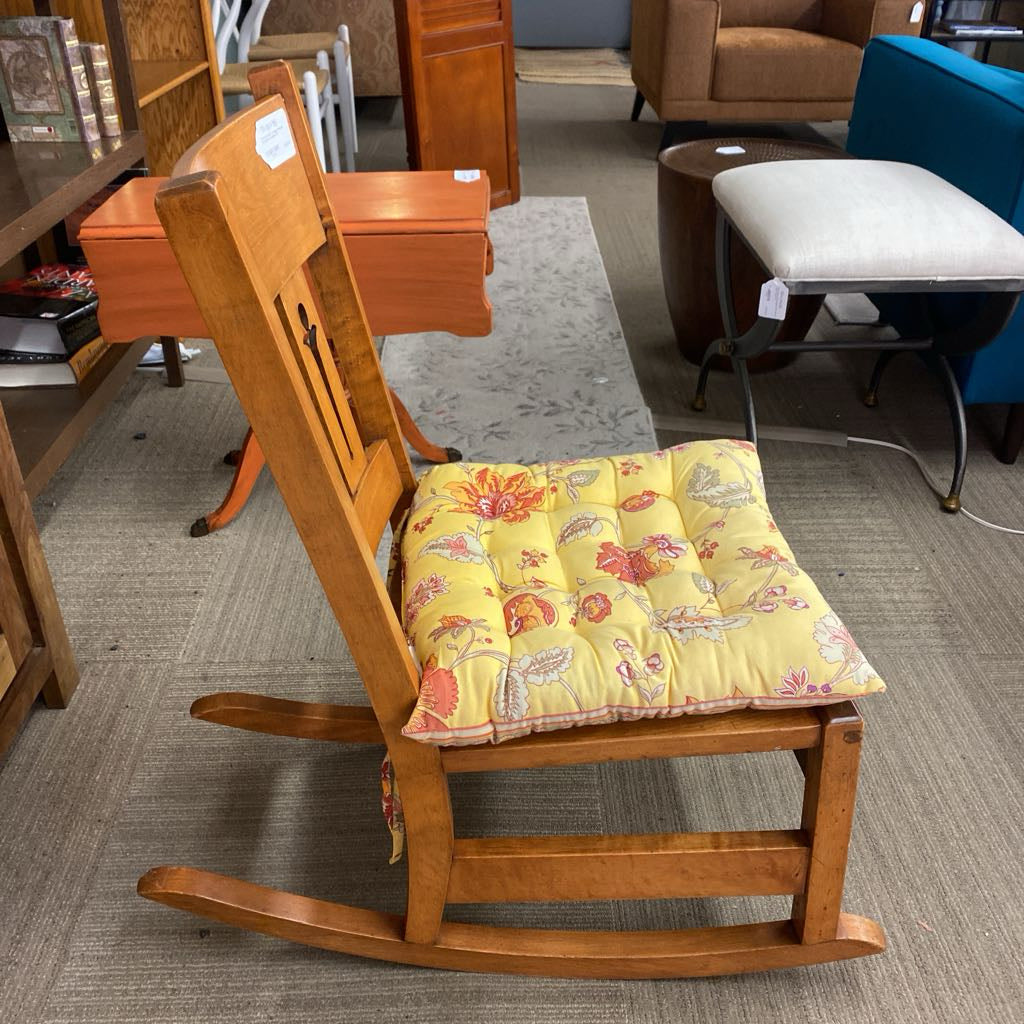 Wooden rocking chair with a yellow floral cushion in a furniture store setting.