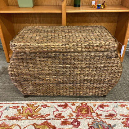 Woven storage basket on a carpeted floor with a wooden shelf in the background