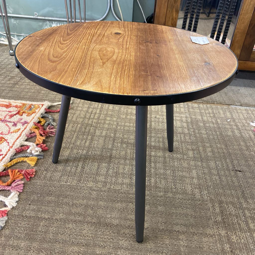 Round wooden table with black metal legs on a carpeted floor