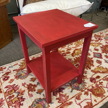 Red side table on a patterned rug with a white pillow in the background
