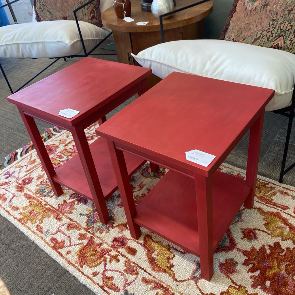 Two red side tables on a patterned rug with cushions in the background.