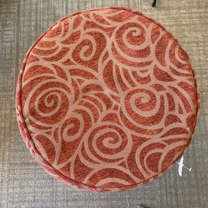 Round cushion with a red and beige pattern on a gray carpet