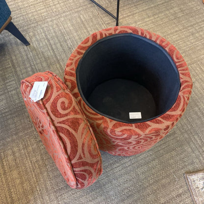 Red patterned ottoman with a black interior on a carpeted floor