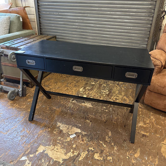 Black desk with two drawers on a wooden floor.