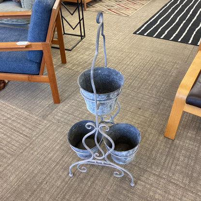 Three-tiered metal plant stand with blue pots on a carpeted floor.