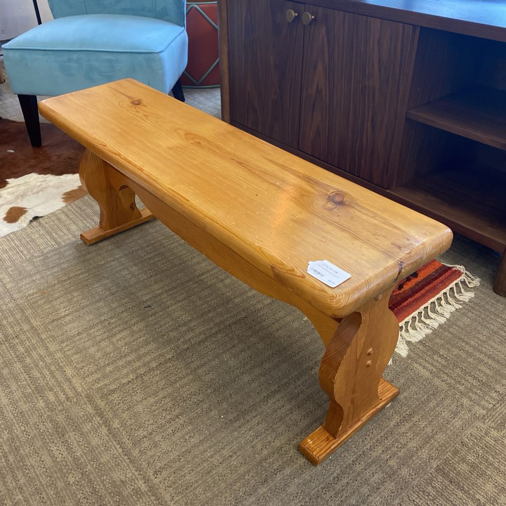 Wooden bench on a carpeted floor with a tag, in front of a piece of furniture.