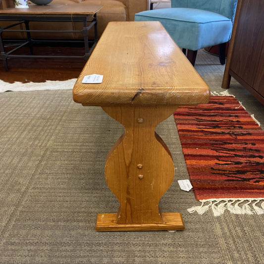 Wooden bench with decorative pedestal base on a carpeted floor
