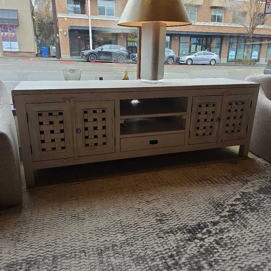 White entertainment console with decorative elements on a patterned rug, with a city street view in the background.