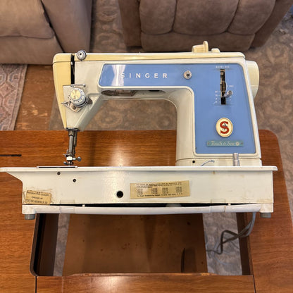 Vintage Singer sewing machine on a wooden surface with a brown couch in the background.
