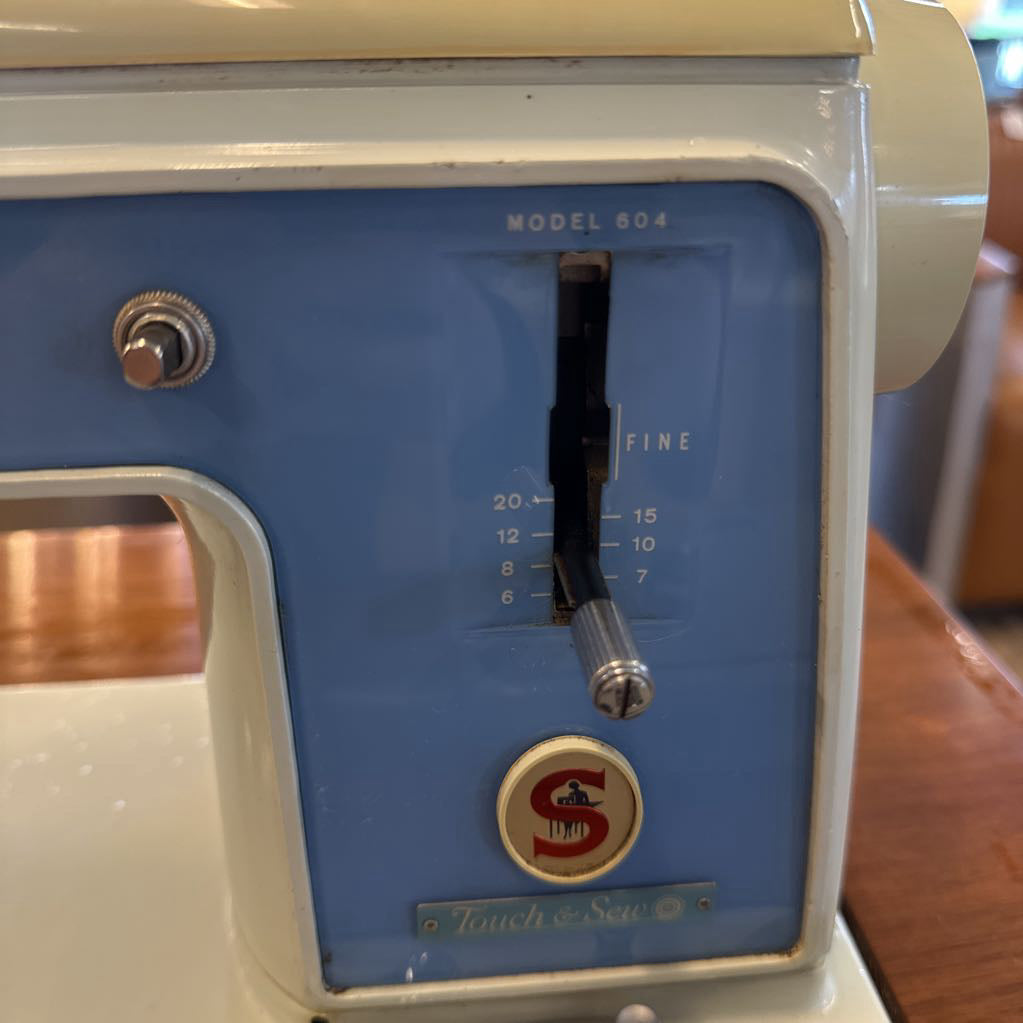 Vintage sewing machine with blue panel and brand logo on a wooden surface