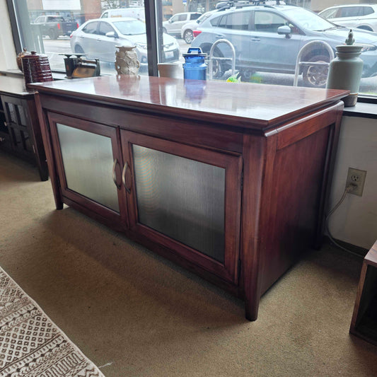 Wooden corner cabinet with glass doors in a room with a window view.