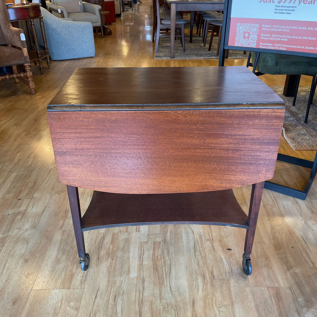 Wooden table with wheels on a wooden floor in a room with chairs and tables.