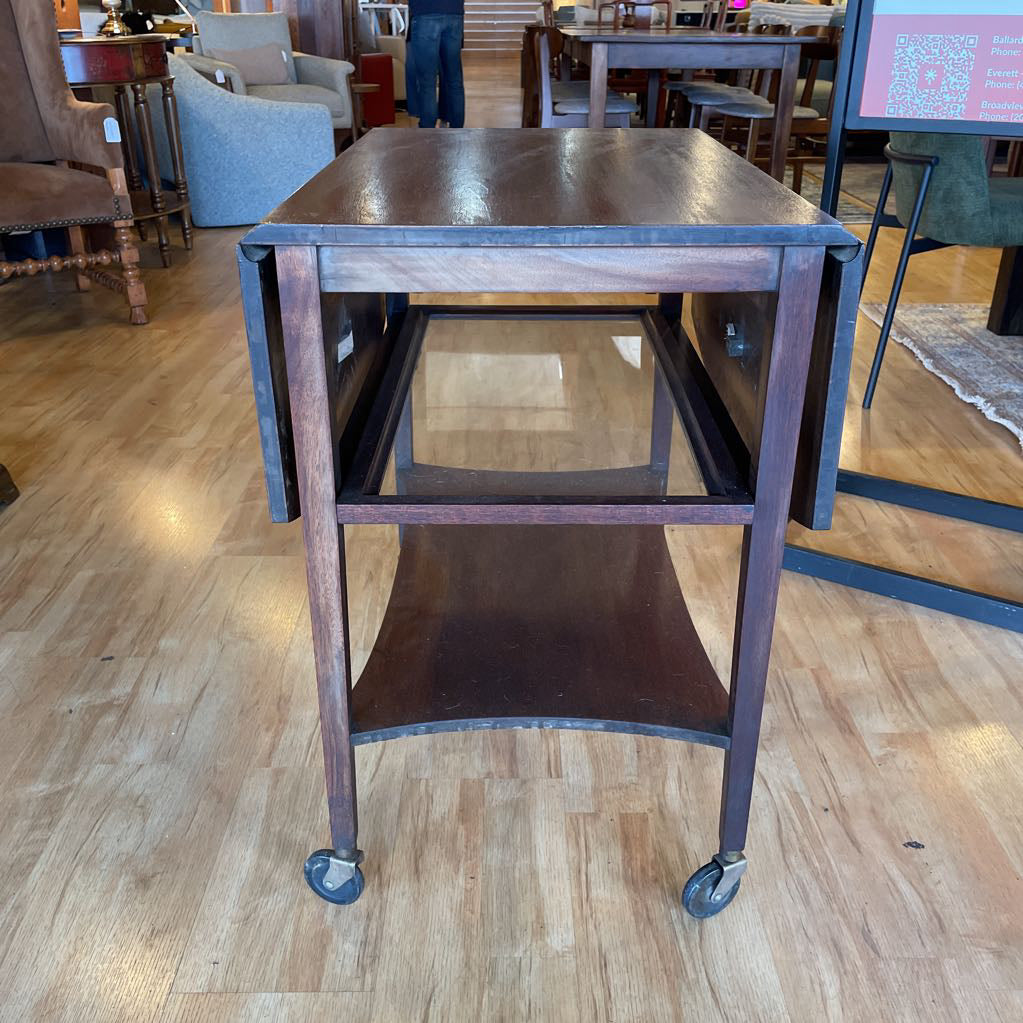 Wooden rolling table on wheels in a room with chairs and tables.