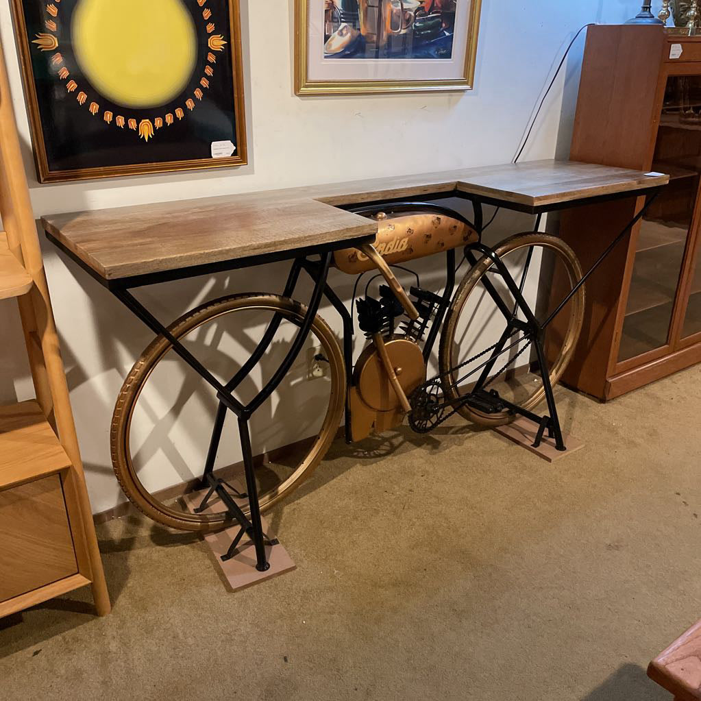 Wooden desk with bicycle wheels as legs in a room with framed pictures on the wall.
