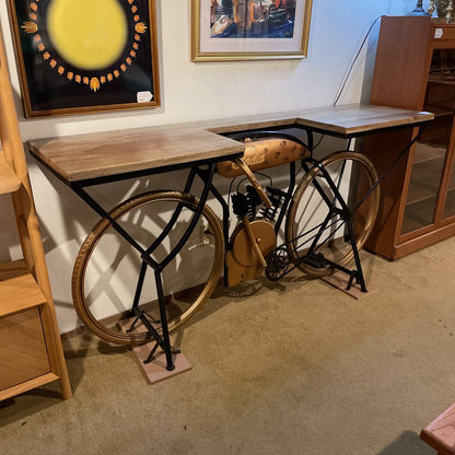 Wooden desk with bicycle wheels as legs in a room with framed pictures on the wall.