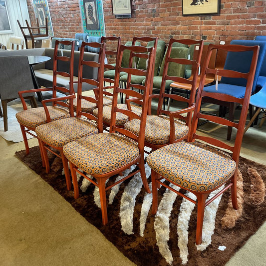 Wooden chairs with patterned seats on a brown rug in a room with brick walls and framed pictures.