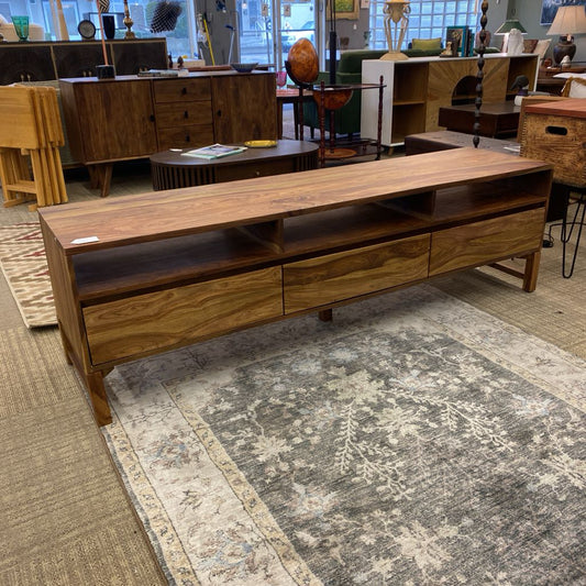 Wooden TV stand in a furniture store with various items in the background